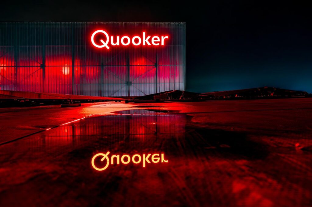 Het rode Quuoker-logo op de gevel van de nieuwe locatie in het donker.